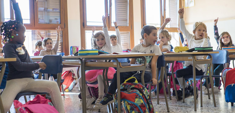 foto bambini sui banchi di scuola con mano alzata